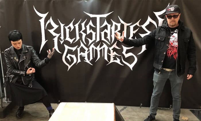 Two people pose in front of a "Rockstar Games" banner. The person on the left wears a black leather jacket and skirt, striking a dynamic pose, while the person on the right sports sunglasses and a cap, pointing outward. Their excitement mirrors the thrill of hitting $1 billion milestones in gaming adventures.