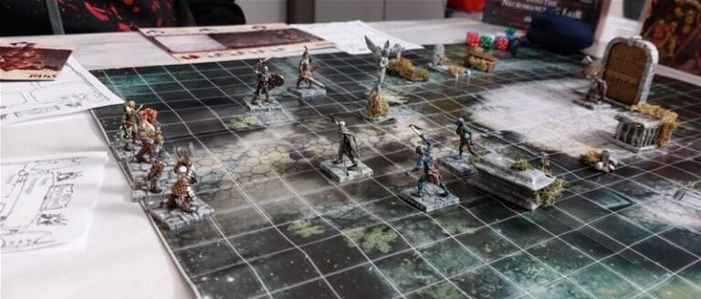 In progress is a tabletop role-playing game by Mantic Games, featuring a grid map with miniature fantasy figures, dice, and game cards. The scene includes a stone archway and weathered ruins, evoking the thrill of Dungeon Adventures while earning positive reviews from players.