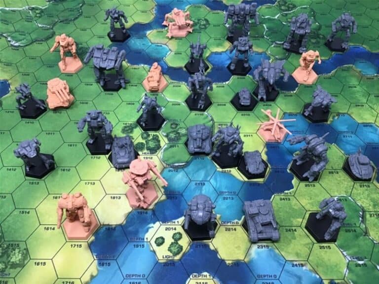 A tabletop game setup features BattleTech Minis, including miniature mech figures on a hexagonal grid map. The map depicts varied terrain in green, blue, and brown, with both gray and orange mechs strategically positioned across the board by Catalyst Game Labs.