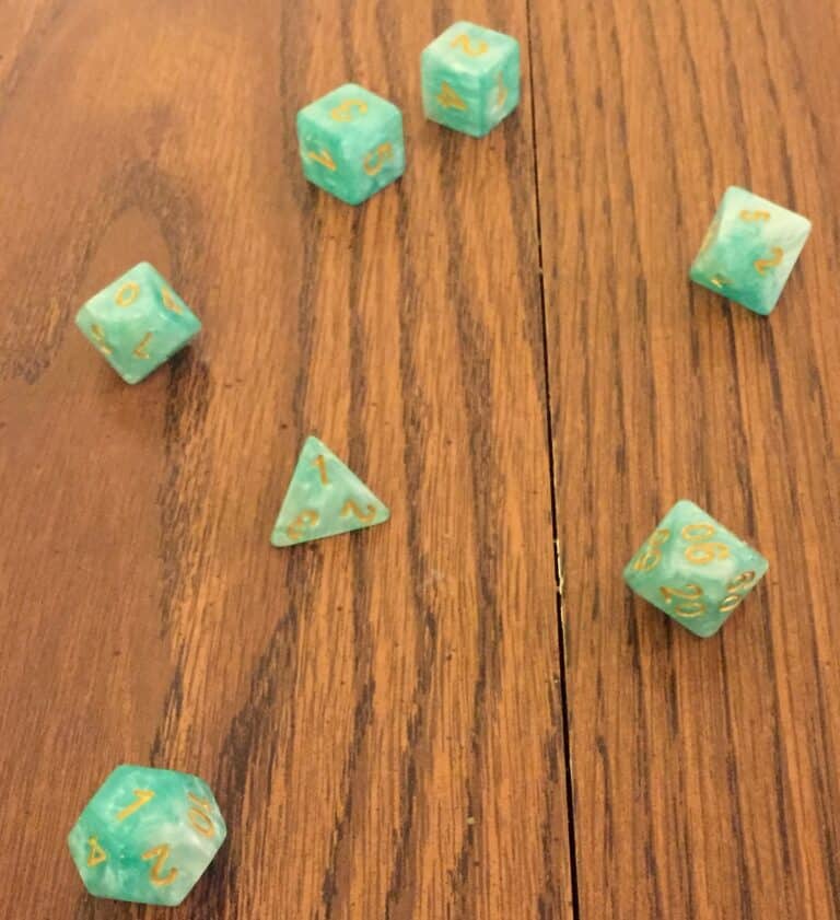A collection of green and gold Kraken Dice, including D4, D6, D8, D10, D12, and D20, scattered on a wooden surface.