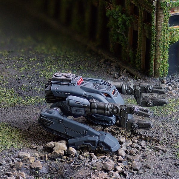 A miniature model of Attila Trackwalker, the futuristic robot with tank-like treads and dual claw arms, is set in a TT Combat diorama. The scene has industrial debris and greenery, creating a post-apocalyptic vibe perfect for WIP Wednesday enthusiasts.