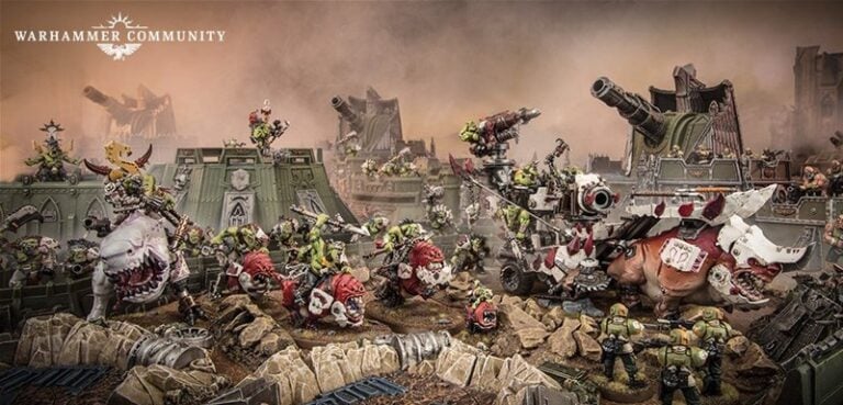 A detailed Warhammer 40k miniatures scene depicts Mozrog Skragbad leading an orc army with various creatures and machines, including tanks and a large boar. The smoky, battle-worn landscape features more armored vehicles and figures, showcasing Games Workshop’s intricate designs.