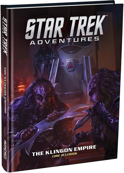 The cover of the "Star Trek Adventures: Klingon Core Rulebook" by Modiphius showcases two Klingon warriors brandishing traditional weapons. A striking Klingon symbol looms in the background, adding to the dark and intense atmosphere.