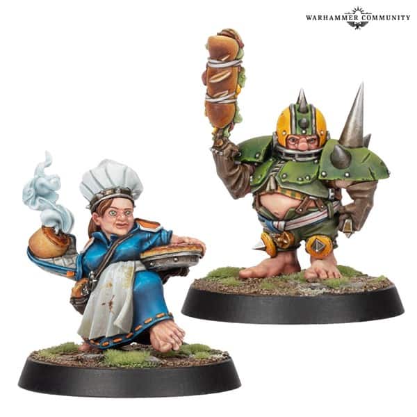 A painted miniature of a cook wearing a chef's hat, holding a steaming pie, stands next to an armored figure with a helmet, raising a sandwich. Both are on round bases with grass details, reminiscent of Star Players from Games Workshop's Blood Bowl universe.