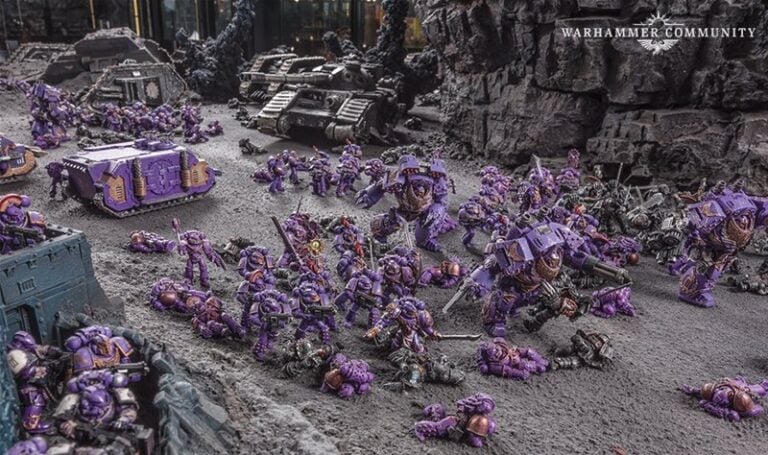 Intricate tabletop scene featuring Warhammer miniatures. Purple-armored Emperor's Children space marines and machinery are engaged in battle on a rocky terrain. Scattered soldiers and vehicles from the Horus Heresy era add to the dynamic, war-like atmosphere.