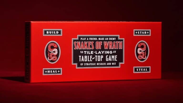 A red boxed tabletop game titled "Snakes of Wrath" is displayed against a dark red background. The box features snake illustrations and text indicating it is a tile-laying game involving building, healing, stabbing, and stealing. This Kickstarter project combines strategy and sabotage to enthrall players.