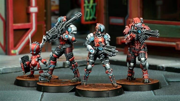Four intricately painted sci-fi miniature figures from the Corvus Belli January Releases stand on round bases. Each figure wears detailed armor in red, blue, and silver tones, holding futuristic weapons. They are positioned in a dynamic urban setting, suggesting a tactical scene.