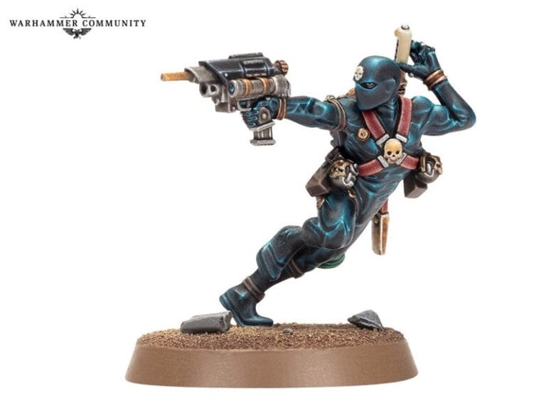 A miniature figure of a masked, blue-clad warrior from the Warhammer universe, possibly inspired by The Horus Heresy, holding a gun in one hand and a scroll in the other. Detailed with skull emblems and equipped with various gear, it poses dynamically on a sandy base.