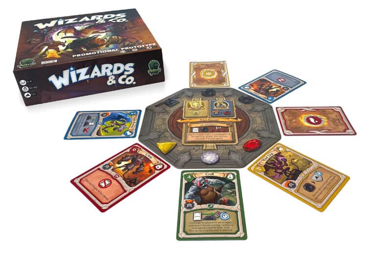 A board game setup with the Kickstarter-backed “Wizards & Co.” box in the top left. Various colorful cards are placed around a circular board with different symbols and tokens, inviting players into a competitive dungeon-raiding adventure.