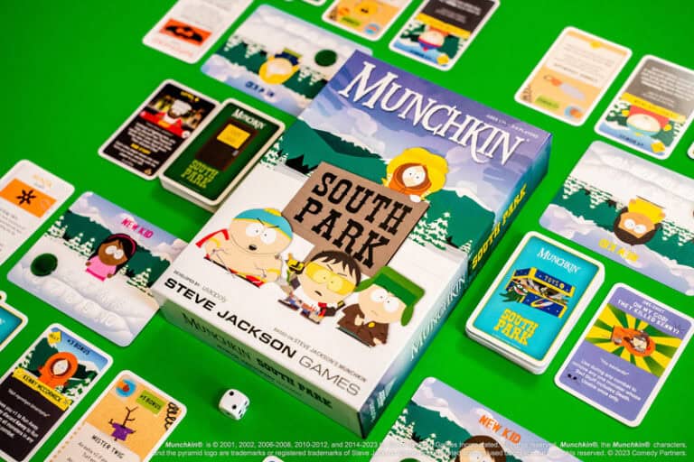 A box of "Munchkin: South Park" sits on a green table, surrounded by game cards sprawled out for a wild ride. The box showcases vibrant cartoon characters from South Park, capturing the essence of the game's quirky adventure.