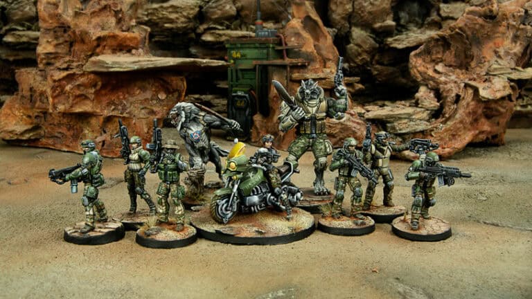 Miniature figures in military attire stand ready with weapons amid rocky terrain, evoking the strategic essence of a tabletop game. A motorcycle figure dominates the center. Perfect for Infinity enthusiasts, this detailed setup is among our anticipated March releases of miniatures.