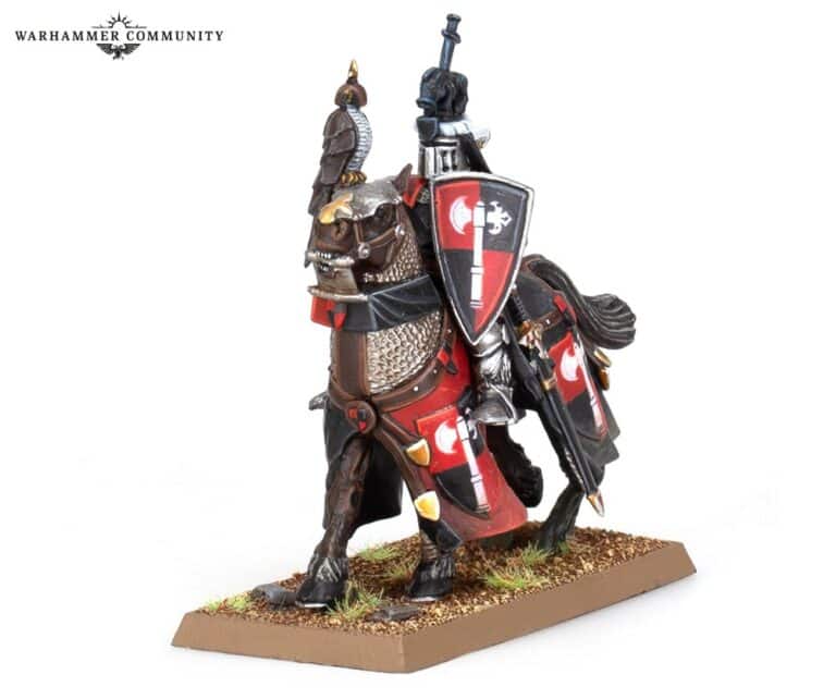 A detailed miniature model of a knight on horseback, reminiscent of Bretonnian Armies, features intricate armor and a lance. The knight's shield displays red and black designs. The horse boasts matching armor and colorful heraldry on a textured base, echoing the classic Warhammer: The Old World style.