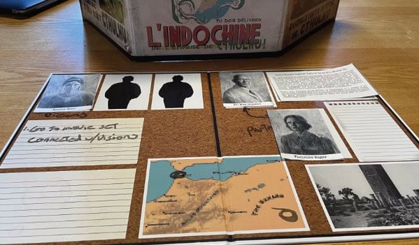 A table displays a corkboard with vintage photos, maps, and handwritten notes. The board, reminiscent of a Call of Cthulhu campaign, features portraits and silhouette cutouts centered around a map of Southeast Asia labeled "L'Indochine," hinting at dark secrets waiting to be uncovered.