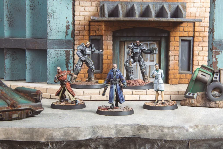 Miniature figures are set in a diorama of a sci-fi urban landscape, reminiscent of Modiphius Entertainment's style. The figures, in futuristic attire with armor and robes, stand on a detailed base featuring a dilapidated vehicle and brick building, echoing the vibes of a Fallout Update.