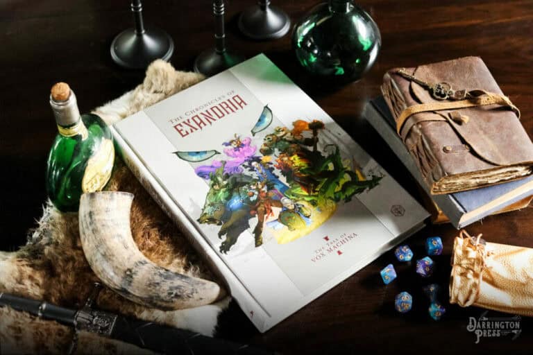 A tabletop scene displays a fantasy-themed book titled "The Chronicles of Exandria: Tale of Vox Machina," surrounded by a leather-bound journal, dice, a green potion bottle, a horn, and other mystical items on a wooden surface.