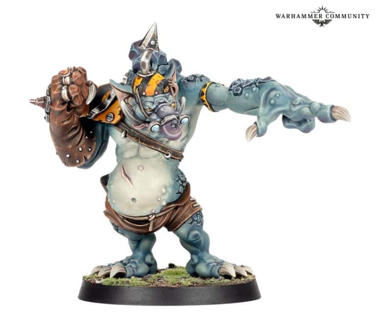 A fantasy ogre miniature from Warhammer, wearing armor and leather attire, stands on a round base. The ogre points forward with a clawed hand and has a fierce expression reminiscent of the legendary Ripper Bolgrot. Its blue-grey skin features intricate details and accessories.