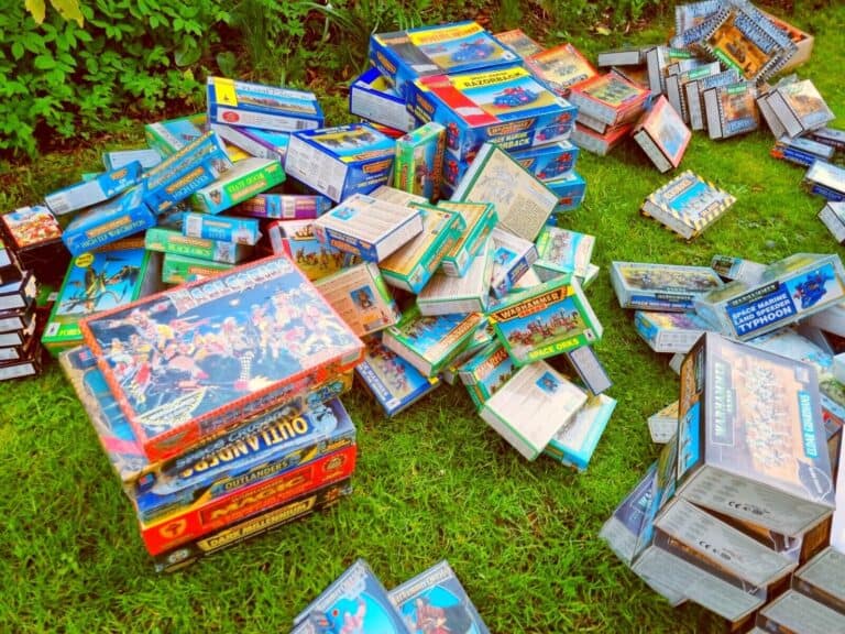 A cluttered assortment of board game boxes scattered on a grassy lawn hints at a vibrant vintage collection in the making. Various colorful covers, some open with contents exposed, revive nostalgia. It's a scene reminiscent of eBay auctions amid lush greenery.