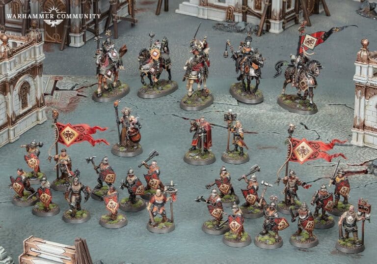 Miniature Warhammer soldiers in ornate armor, some representing the Age of Sigmar and Cities of Sigmar factions, wield weapons while holding red banners. They are intricately displayed on a detailed model battlefield with miniature buildings.