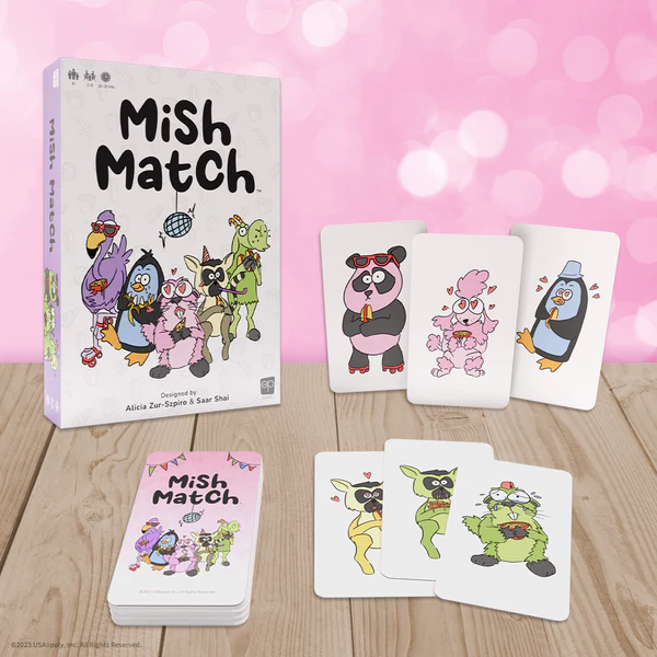 A card game titled "Mish Match" is displayed on a wooden surface, inviting you to dive into this party game. Brought to you by Op Games, the game box and cards showcase playful cartoon animals in quirky costumes against a pink bokeh background, with fanned-out cards beside the box.