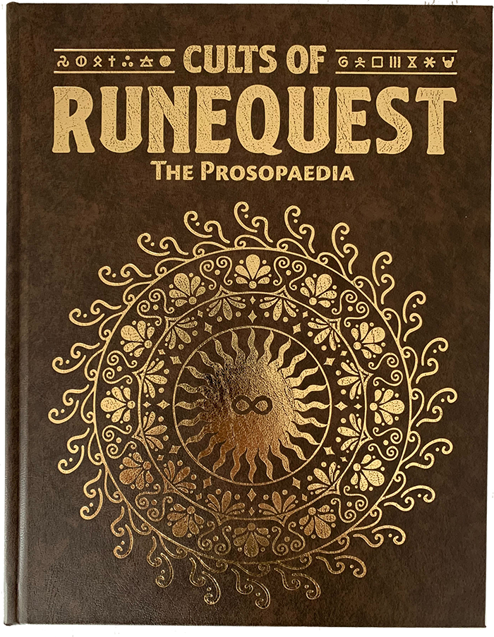 The image showcases the cover of Chaosium's "Cults of RuneQuest: The Prosopaedia." It features a dark brown backdrop with ornate golden designs, centered around a sun-like emblem with a face, surrounded by intricate symbols.
