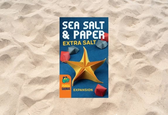 Board game cover for "Sea Salt & Paper: Extra Salt - Mini Expansion" on a sandy background. Features a gold origami starfish and red-blue paper shapes. Pandasaurus Games logo at the bottom.