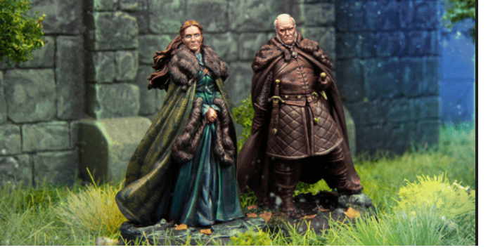 Two fantasy figurines stand on grass against a stone wall backdrop, reminiscent of a scene from Game of Thrones. The left figure is a woman in a long green dress and fur-trimmed cape. The right figure is a bald man in a brown quilted outfit and cape, both looking forward as if vying for the Iron Throne.