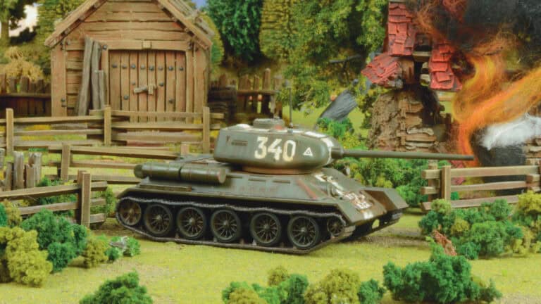 A model tank labeled "340" stands in a miniature battlefield scene, embodying the intensity of tank warfare. It is surrounded by greenery, a wooden fence, and a rustic cabin. One corner reveals flames engulfing a building, reminiscent of an Achtung Panzer diorama's engaging wartime atmosphere.