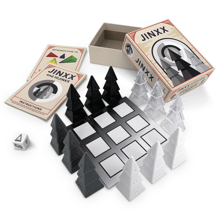 The JINXX board game set features black and white tree-shaped pieces on a grid board. A box marked "JINXX" includes a symbol-adorned die, instruction booklets titled "JINXX and NINJAS," and complements the whimsical style of Looney Pyramids from Looney Labs.