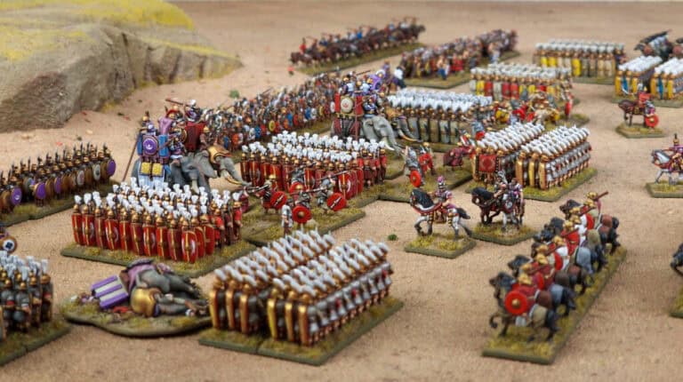 A detailed tabletop wargame setup from the Hail Caesar Series features miniature Roman armies in formation, with soldiers, cavalry, and elephants on a desert-like terrain. Vibrant colors depict historic battle scenes of the Punic Wars, with various units positioned strategically.