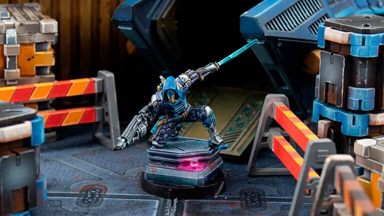 In May, the new releases from Infinity Miniatures showcase a futuristic armored figurine in blue and silver, dynamically posed with a glowing blade. Surrounded by crates and barriers, the scene exudes an action-packed, high-tech ambiance.