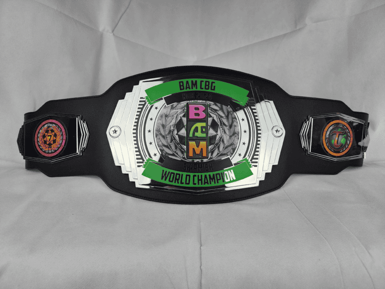 A championship belt with a black strap and silver details is displayed in classic pro wrestling style. The center showcases "BAM CBG WORLD CHAMPION" with green accents and a colorful logo. Vibrant side plates feature unique designs, including a pink circle and another with a "T".