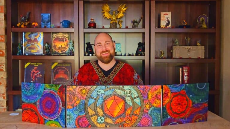 A person with a beard sits behind a colorful DM screen featuring intricate designs, clearly marking them as one of the professional Dungeon Masters. They're smiling in their red patterned shirt, while a bookshelf behind them showcases an array of Wizards of the Coast fantasy books, figurines, and decorations.