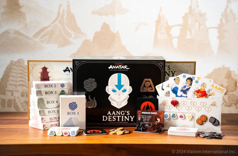 The Op Games presents 'Aang's Destiny,' an 'Avatar: The Last Airbender' board game set elegantly displayed on a wooden table. Featuring game boxes, cards, coins, character pieces, and a decorative board in the background, it's perfect for fans eager to explore Aang's journey.