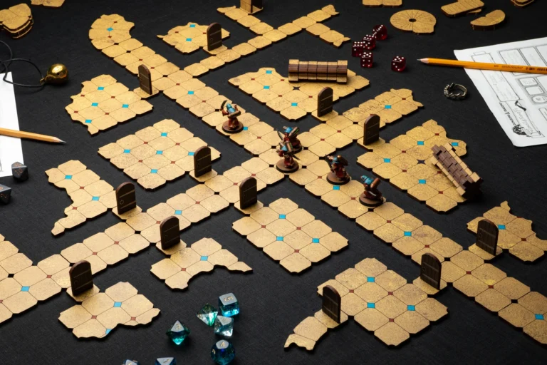 A tabletop role-playing game setup features a Pre-Painted Dungeon Tile Set, forming a dungeon pathway known as the Mad Wizard's Hall. Miniature figures stand among dice, pencils, and character sheets, with various door and wall markers ready for the adventure supported by Gamefound.
