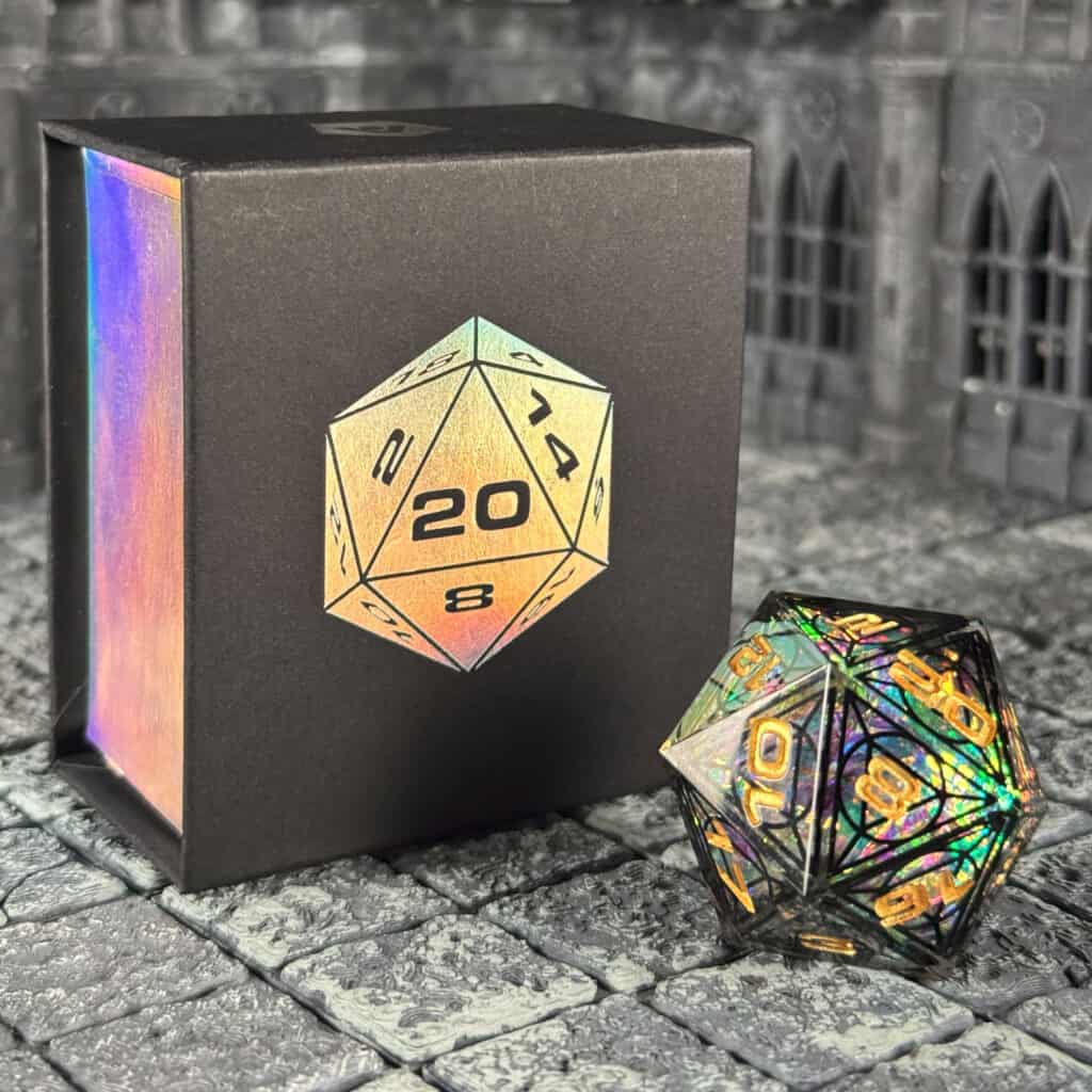 A shiny, Cathedral-inspired 20-sided die with colorful reflections sits next to a black box featuring a similar holographic design. The background, reminiscent of an RPG dice setting, is a textured stone surface.