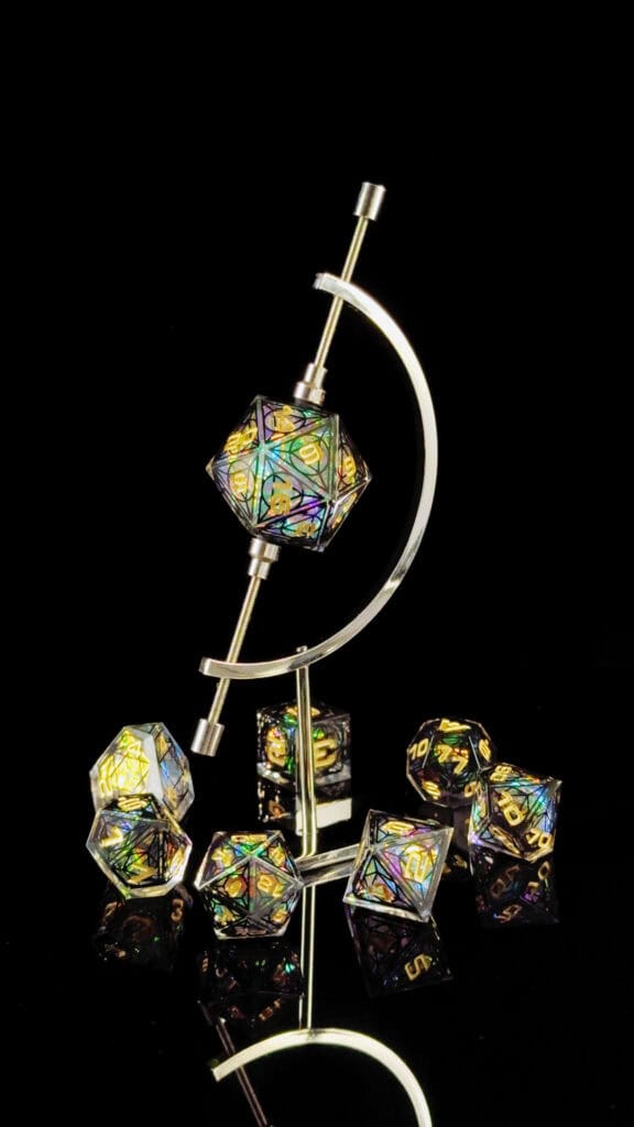 A set of iridescent Cathedral Dice, including a large die on a metal stand and several smaller ones, displayed on a reflective black surface. These Gothic-inspired RPG dice feature colorful geometric patterns, creating a vibrant and striking visual effect.