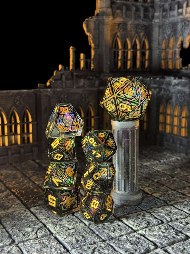 A collection of gothic-inspired RPG dice with colorful, reflective patterns is stacked on a medieval-themed stone floor. Some dice rest atop a small, ornate column amidst the glow of cathedral-like architecture.