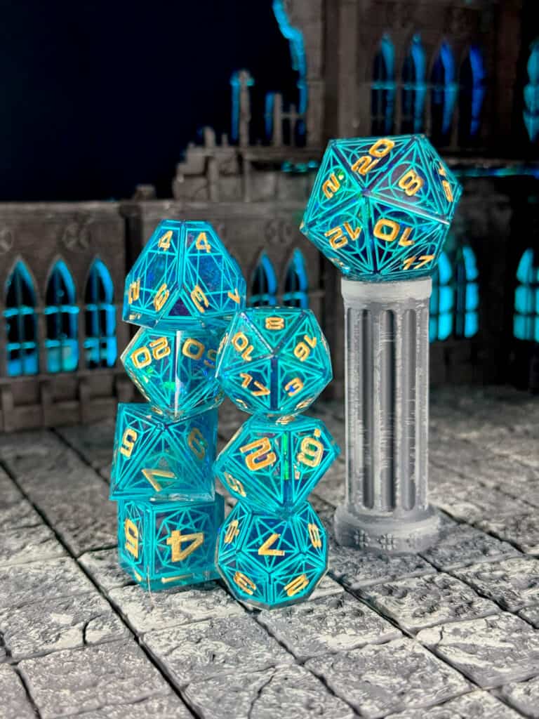 A set of translucent blue twenty-sided Cathedral Dice with glowing turquoise numbers is arranged on a weathered stone floor. In the background, there's a model of gothic architecture and a column topped with another die, evoking the aura of Aether Objects in an enchanted realm.