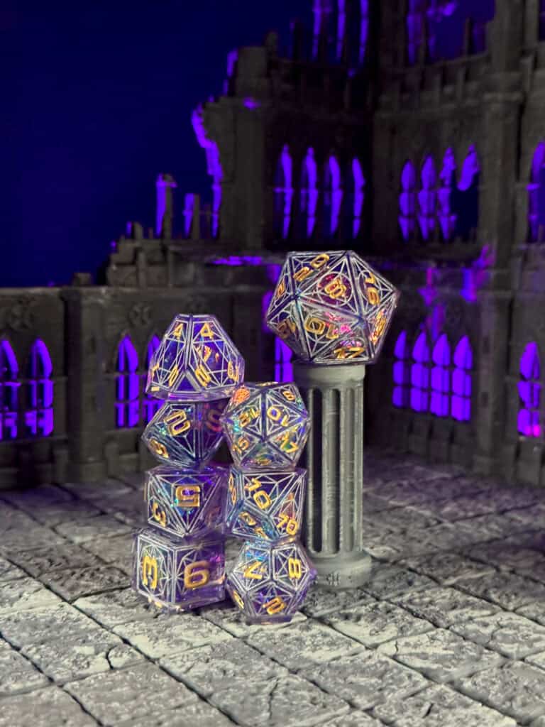 A set of translucent Cathedral Dice with colorful numbers is displayed in a dark, gothic scene. The dice are stacked on a stone floor beside a column, with a purple-lit ruined building in the background.